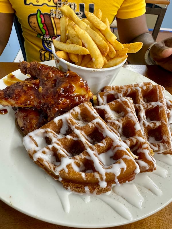 A plate of chicken and waffles covered in white chocolate syrup.
