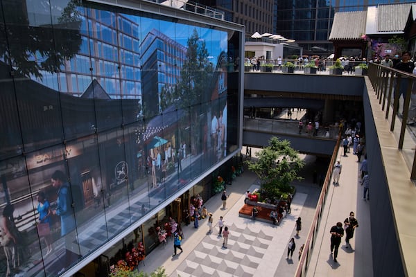People tour by a projector screen promoting a newly opened outdoor Hutong style shopping mall, in Beijing, Monday, May 26, 2025. (AP Photo/Andy Wong)