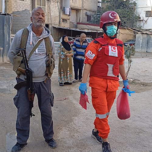 A Hamas gunman, left, stands next of a Palestinian rescue man who carries a bag with body remains, near the scene where an Israeli strike hit on Tuesday night the Ein el-Hilweh Palestinian refugee camp, in the southern port city of Sidon, Lebanon, Wednesday, Nov. 19, 2025. (AP Photo/Mohammed Zaatari)