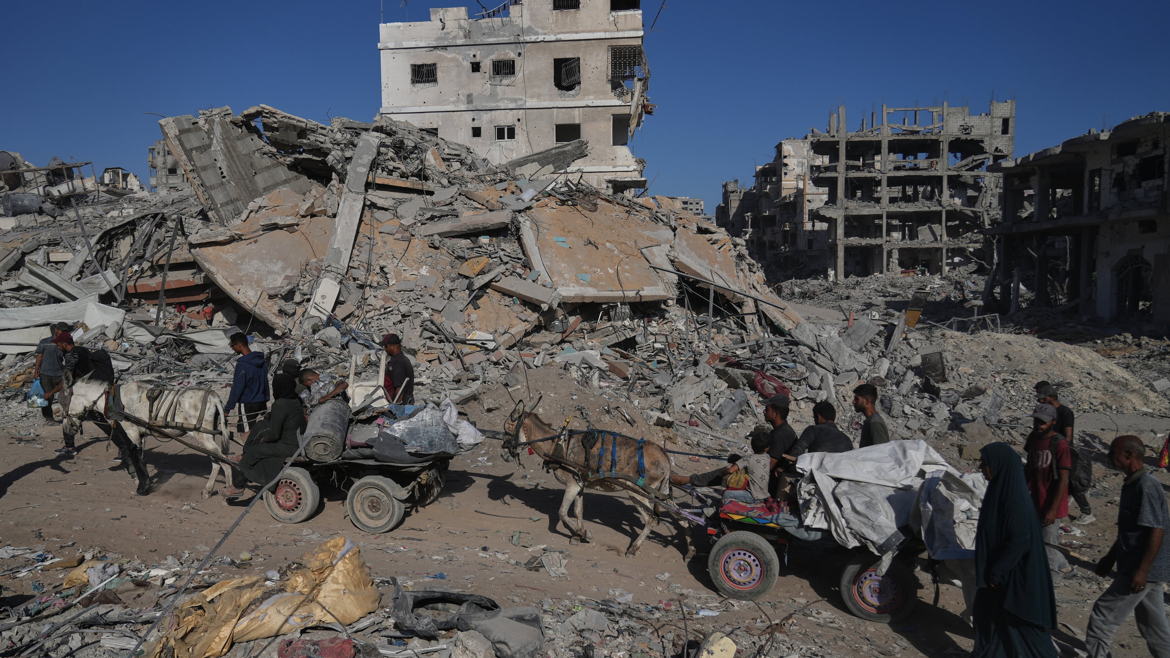 Displaced Palestinians ride donkey carts loaded with belongings past destroyed buildings in Gaza City, Saturday, Oct. 11, 2025, after Israel and Hamas agreed to a pause in their war and the release of the remaining hostages. (AP Photo/Abdel Kareem Hana)