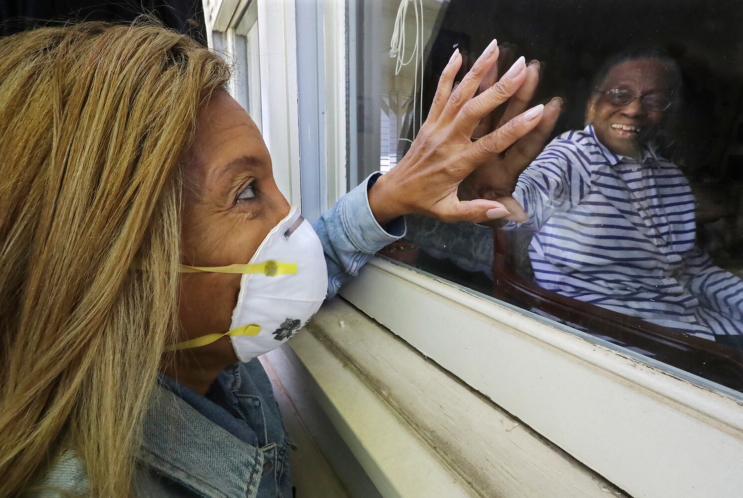 April 28, 2020 Carrollton: Camilla White visits her mother Lillian Barber, 90, from outside seeing her through the window while touching fingertips through the glass at Cottage Landing Assisted Living on Tuesday, April 28, 2020, in Carrollton. White didn’t discover there had been several deaths at the home from coronavirus and a significant outbreak until seeing the info on a state website and said that before the outbreak “I would go inside and just lay my head in her lap, but I can’t do none of that anymore.”      Curtis Compton ccompton@ajc.com