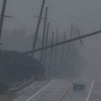 A vehicle drives near a downed utility pole dangling above Mamalahoa Highway during Hurricane Lala near Ocean View, Hawaii, Saturday, Aug. 15, 2026. (Stephen Lam/San Francisco Chronicle via AP)