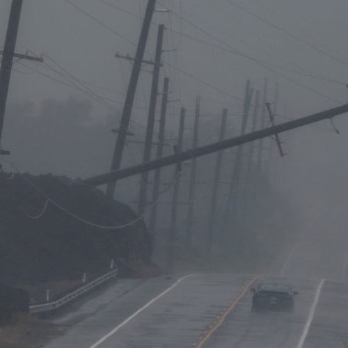 A vehicle drives near a downed utility pole dangling above Mamalahoa Highway during Hurricane Lala near Ocean View, Hawaii, Saturday, Aug. 15, 2026. (Stephen Lam/San Francisco Chronicle via AP)