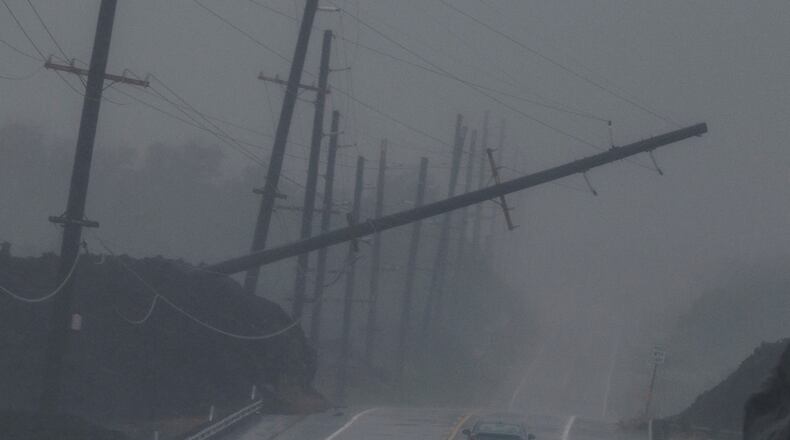 A vehicle drives near a downed utility pole dangling above Mamalahoa Highway during Hurricane Lala near Ocean View, Hawaii, Saturday, Aug. 15, 2026. (Stephen Lam/San Francisco Chronicle via AP)