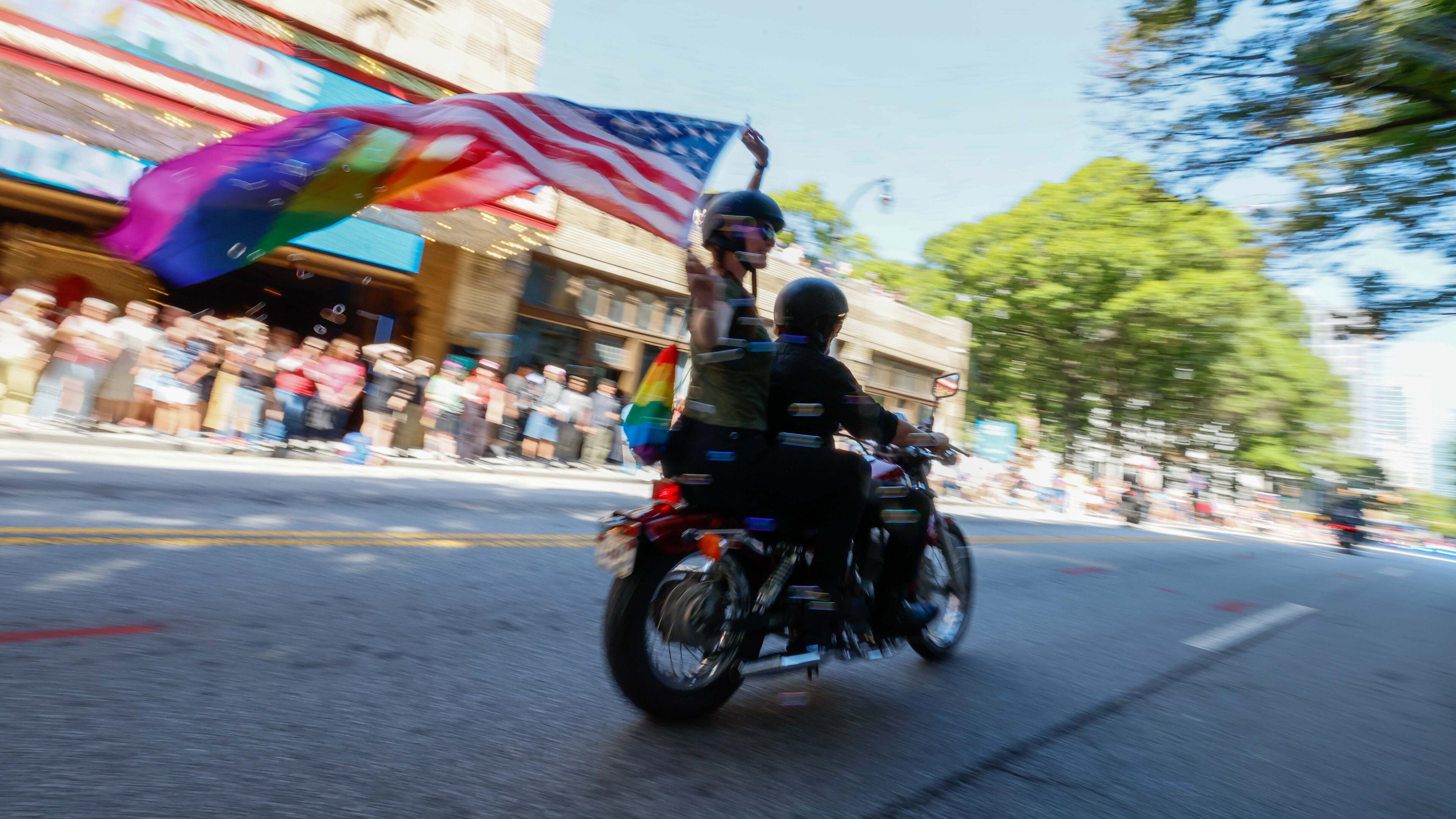 Margaret Tilson carries an American Pride flag as Caroline Smith drives the motorcycle at the beginning of the annual Pride Parade in Atlanta on Sunday, Oct. 13, 2024. (Miguel Martinez/AJC)