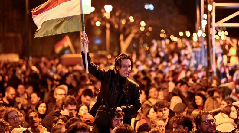 A man waves a Hungarian flag as he celebrates in the streets after the announcement of partial results of the Hungarian parliamentary in Budapest, Hungary, Sunday, April 12, 2026. (AP Photo/Denes Erdos)