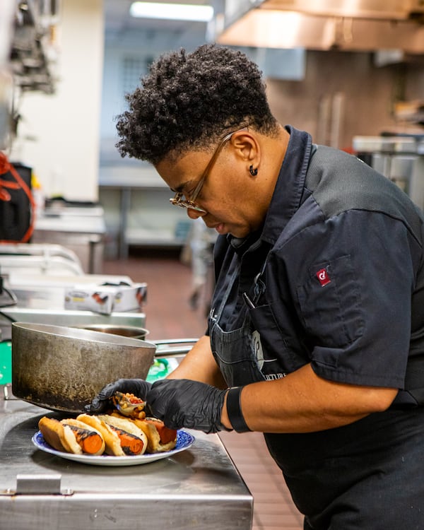 Chef Michele Tompkins prepares a loaded carrot "hot dog" at Chow a La Carte in the Uptown Atlanta development. (Aaliyah Man for the AJC)