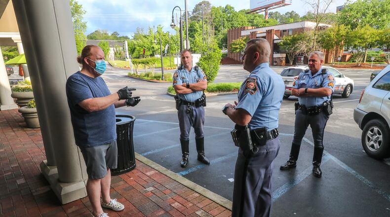 Barber and owner of Chris Edwards wears a mask (left) as he talks with GSP Troopers who were responding to a complaint call that there was a crowd gathering at the shop at Peachtree Battle Barber Shop at 2333 Peachtree Road in Atlanta on Friday, April 24, 2020. The Troopers found the business in compliance.