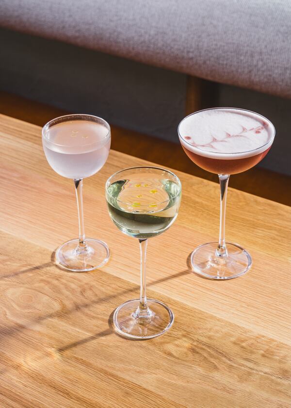 Three cocktails stand in long-stemmed cocktail glasses, one cloudy, one purple with a white foam cap and one perfectly clear.