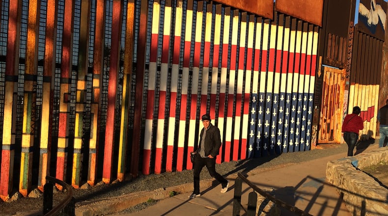People pass graffiti along the border structure in Tijuana, Mexico, Wednesday, Jan. 25, 2017. President Donald Trump moved aggressively to tighten the nation's immigration controls Wednesday, signing executive actions to jumpstart construction of his promised U.S.-Mexico border wall and cut federal grants for immigrant-protecting "sanctuary cities." (AP Photo/Julie Watson)