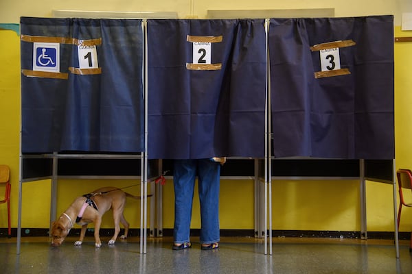 A dog on a leash waits as its owner votes in a booth for referendums on citizenship and job protections, at a polling station in Milan, Italy, Sunday, June 8, 2025. (Claudio Furlan/LaPresse via AP)