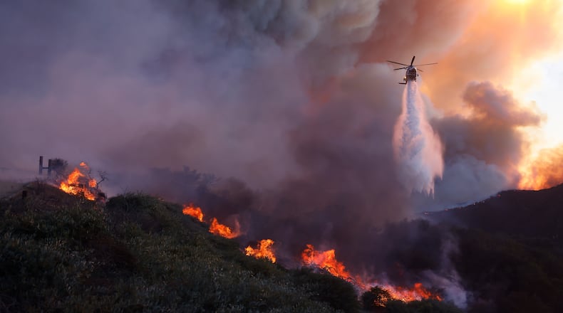 FILE - Water is dropped by helicopter on the advancing Palisades Fire in the Pacific Palisades neighborhood of Los Angeles, Jan. 7, 2025. (AP Photo/Etienne Laurent, File)