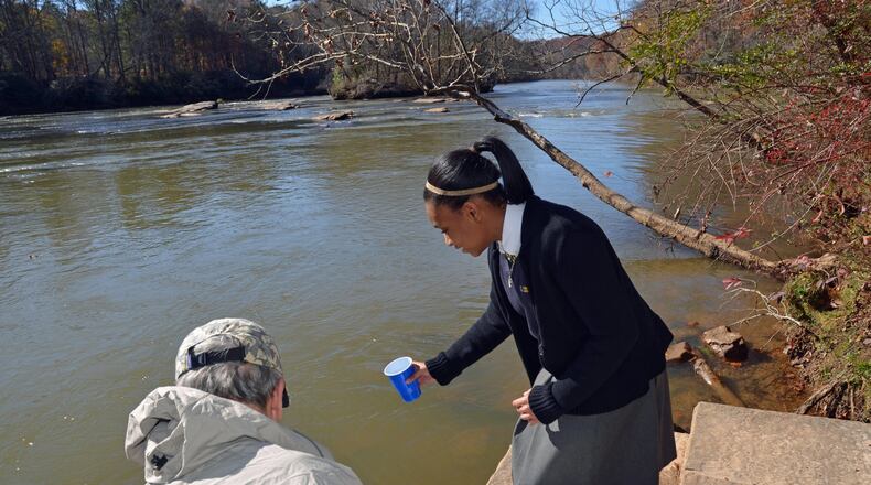 Cristo Rey science student Jasmine Mitchell assists Jim Byrd of the Upper Chattahoochee chapter of Trout Unlimited release trout into the river near Peachtree Corners. Students at the Midtown school raised about 250 trout to help the organization’s conservation efforts. Photo credit: Sylvia Small.