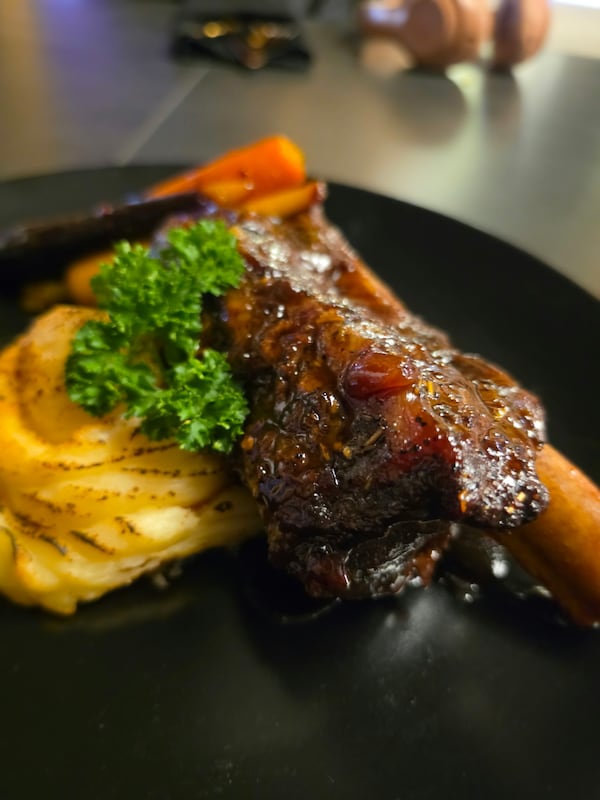 Beef short rib with carrots and mashed potatoes on a black plate