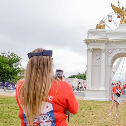 Visitors take photos at the Great American State Fair on the National Mall, with the ferris wheel and a model of the triumphal arch in the background, Thursday, July 9, 2026, in Washington. (AP Photo/Mariam Zuhaib)