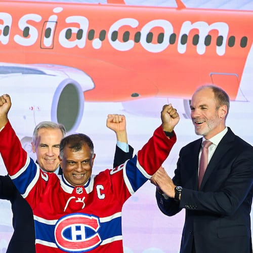 Canada's Prime Minister Mark Carney, left, and Lars Wagner, CEO, Airbus Commercial Aircraft, right, cheer on AirAsia CEO Tony Fernandes, centre, during an event at the Airbus A220 Delivery Center in Mirabel, Que., Wednesday, May 6, 2026, where AirAsia placed a landmark order for 150 Airbus A220 aircraft. (Graham Hughes/The Canadian Press via AP)