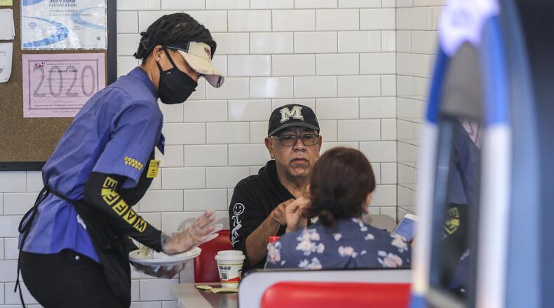 Now that stay-at-home orders have been lifted in Georgia, restaurant servers like Waffle House’s Miss D (left) are donning masks and gloves to protect their patrons. JOHN SPINK / JSPINK@AJC.COM