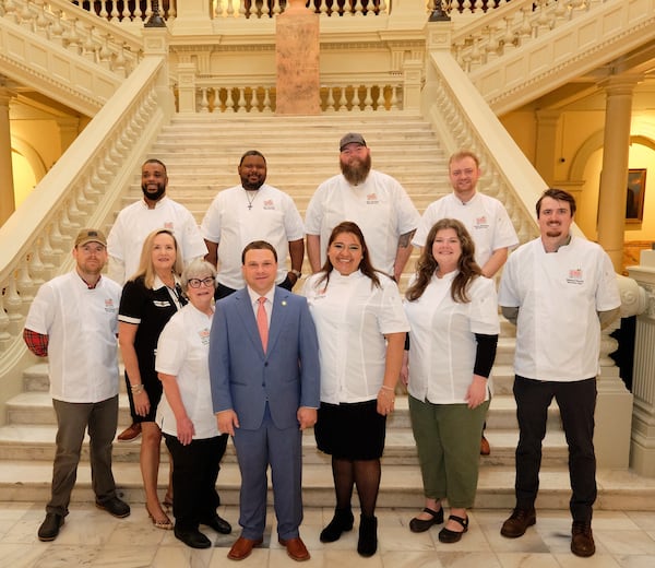 Nine chefs in chef coats stand with two administrators in business suits in front of a grand staircase in the Georgia Capital Building.