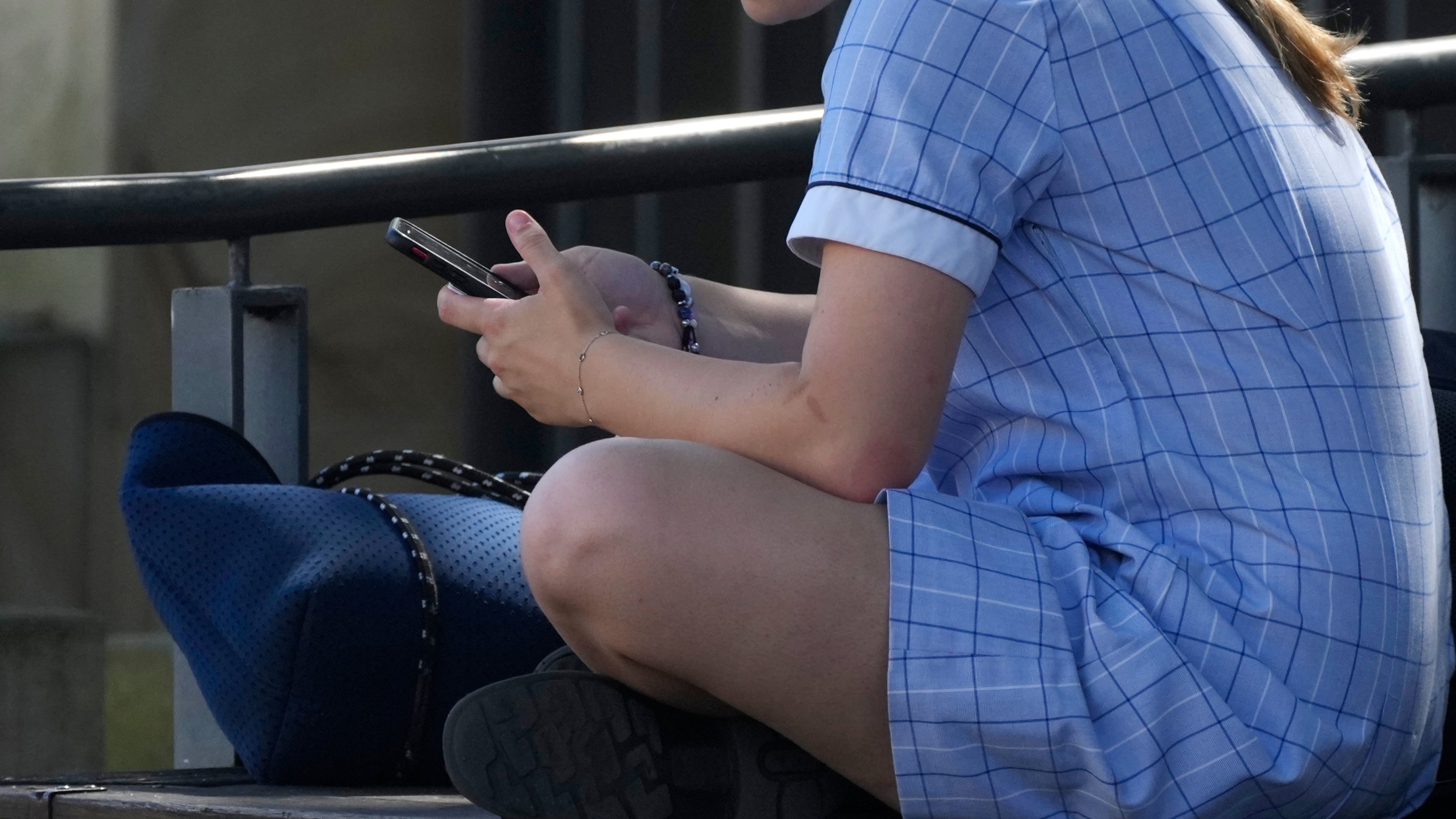 FILE - A young girl uses her phone while sitting on a bench in Sydney, Nov. 8, 2024. (AP Photo/Rick Rycroft, File)