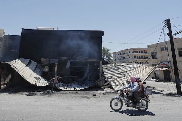 Syrian citizens ride in front of a shop that was burned during clashes between Syrian government forces and Druze militias on the outskirts of Sweida city, southern Syria, Wednesday, July 16, 2025. (AP Photo/Omar Sanadiki)