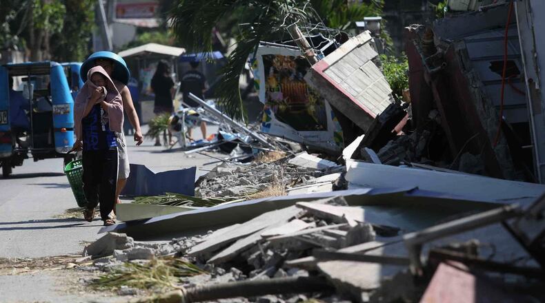 Residents walk past debris from a damaged building in General Santos, southern Philippines, Thursday, June 11, 2026, following Monday's powerful earthquake. (AP Photo/Basilio Sepe)