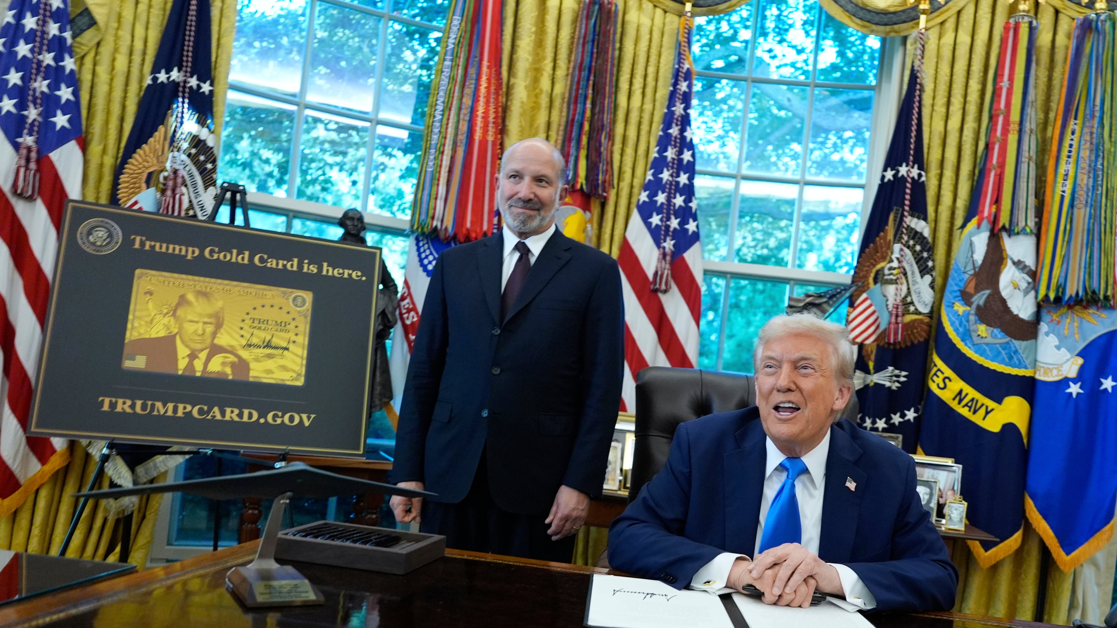 President Donald Trump speaks as Commerce Secretary Howard Lutnick listens alongside a poster of the Trump Gold Card in the Oval Office of the White House, Friday, Sept. 19, 2025, in Washington. (AP Photo/Alex Brandon)