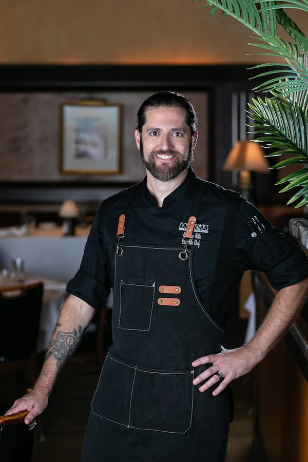 A chef stands in a steakhouse dining room wearing a denim apron.