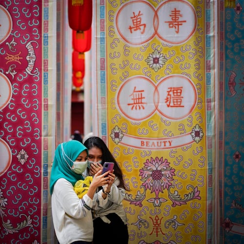 FILE - Two Malay girls check a mobile phone at a fabric installation decoration at Kwai Chai Hong, the Chinatown area in downtown Kuala Lumpur, Malaysia, Tuesday, March 30, 2021. (AP Photo/Vincent Thian, File)