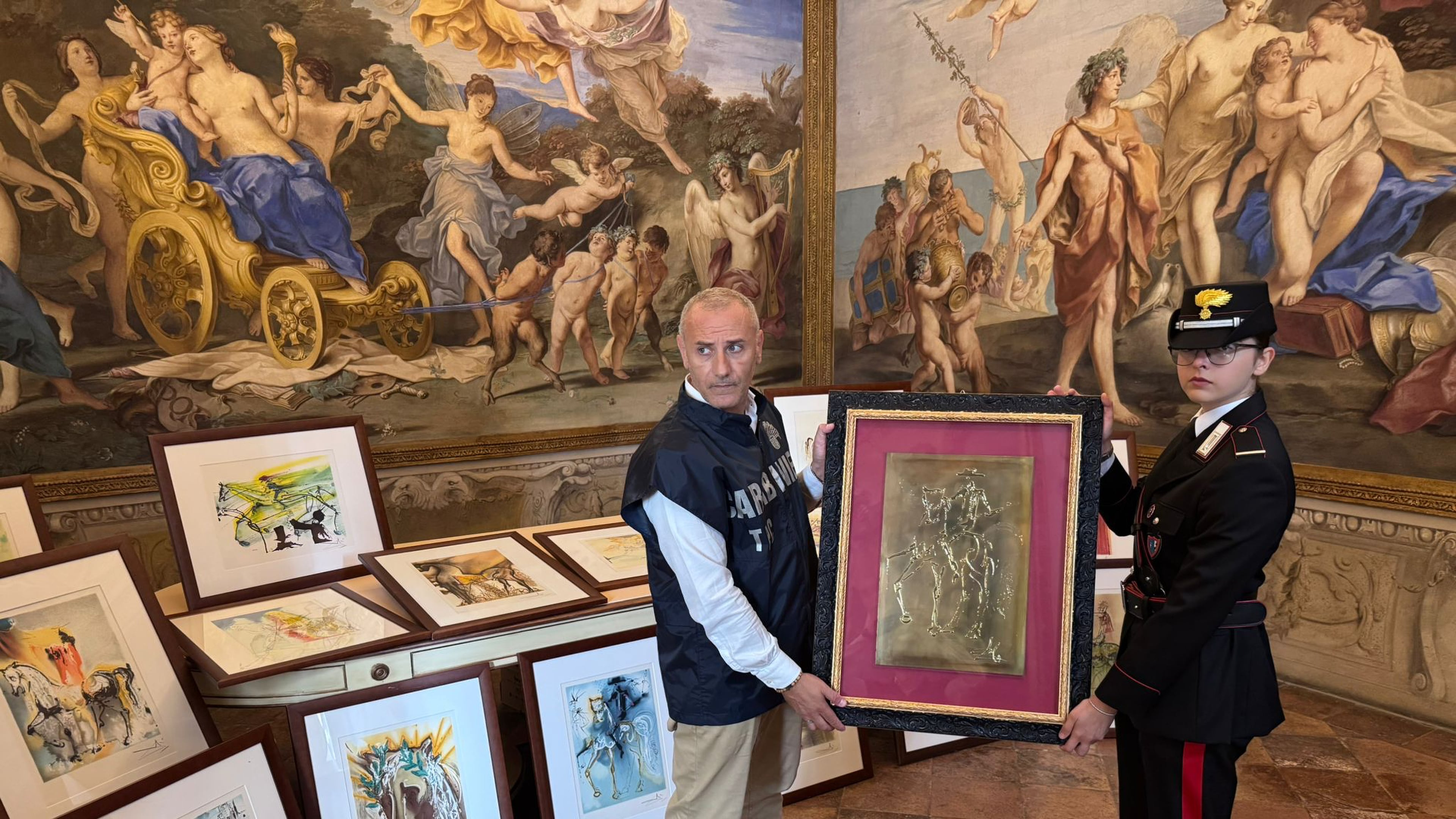 In this handout photo released Wednesday, Oct. 1, 2025 by Italy's Carabinieri Cultural Heritage Protection Command, two officers pose with some of the 21 artworks from the exhibition "Dali. Between Art and Myth" that were seized on suspicion of being fakes, in Parma, northern Italy, Tuesday, Sept. 30, 2025. (Carabinieri Cultural Heritage Protection Command via AP)