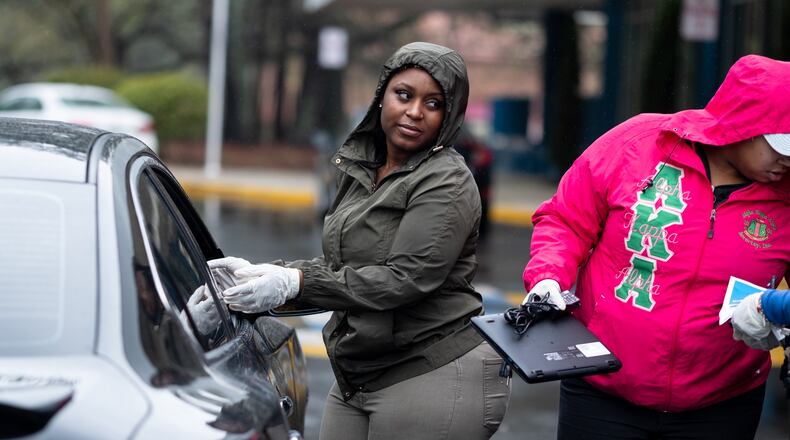 Diamond Parks, left, and Kydeia Mahaffey-Jones, both paraprofessionals at Harper-Archer Elementary School, assign a computer to a student who came to pick it up from the school on March 24, 2020. The school was issuing devices to students so they could continue studying during the coronavirus pandemic. Ben@BenGray.com for the Atlanta Journal-Constitution