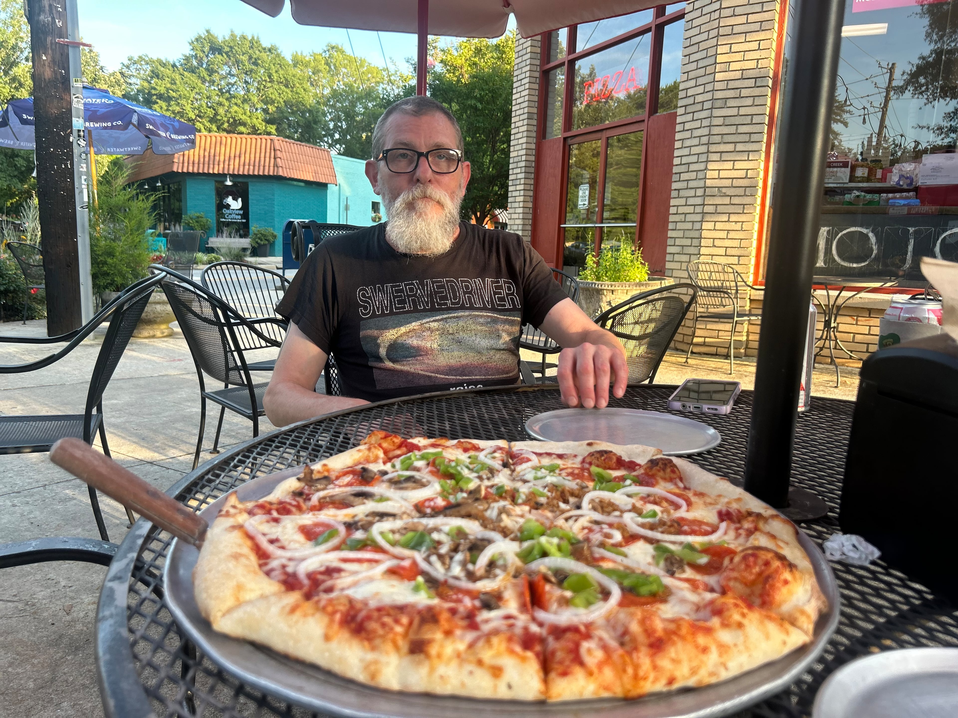 Chad Dumas, a prep cook at Mojo Pizza N' Pub, sits outside the restaurant with a chef's favorite Hurricane pizza on Thursday, June 19, 2025. (Gray Mollenkamp/AJC)