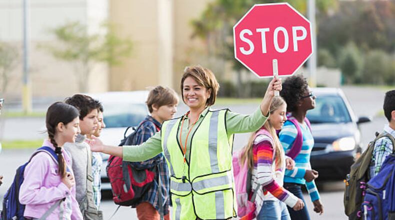 A school crossing guard helps children walk across street. The Canton Police Department has begun automated enforcement of speeding in school zones. CONTRIBUTED