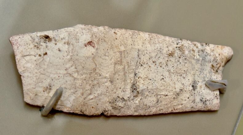 An image of the portion of a Clovis point or spear tip from around 9,000 B.C., which was found in 1935 during excavations at what is now the Ocmulgee Mounds National Historical Park in Macon. It is now on display in the park's visitor center and is shown here, secured to a panel by tiny prongs, enclosed in an observation case. (Joe Kovac Jr./AJC)