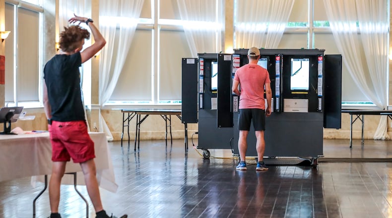 With a light morning voter turnout poll worker, Gamble Everett (left) watches the first voter, Reese McCraine (right) cast his ballot for runoff elections at Park Tavern in Atlanta on Tuesday, June 21, 2022. (John Spink / John.Spink@ajc.com)
