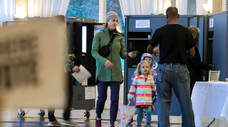 Emily Taylor with daughters Grace, 3, and Margaret, 5, gives her ballot access card to poll worker Errol Webb on on Tuesday at the Park Tavern in Atlanta. (John Spink / John.Spink@ajc.com)