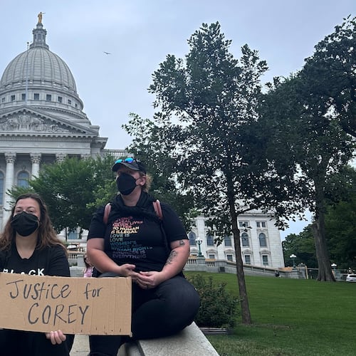 Lilly Nimmer, left, and Reba Bergmann, right, hold a sign to protest the police shooting of Corey Ruiz outside of the Wisconsin state Capitol during the weekly farmers market on Saturday, July 25, 2026, in Madison, Wisconsin. (AP Photo/Scott Bauer)