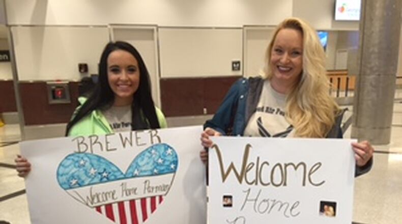 Noel (left) and Mary Ann Rivest, Jonathan Brewer’s sister and mother, hold signs and wear T-shirts welcoming the airman home for the holidays. DAN KLEPAL / DKLEPAL@AJC.COM