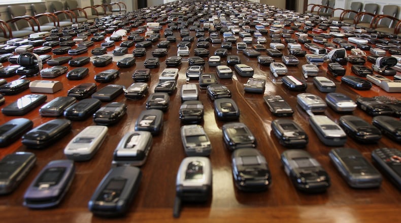 Hundreds of confiscated cellphones are laid out on a conference table at the state Department of Corrections. (AJC file / Vino Wong)