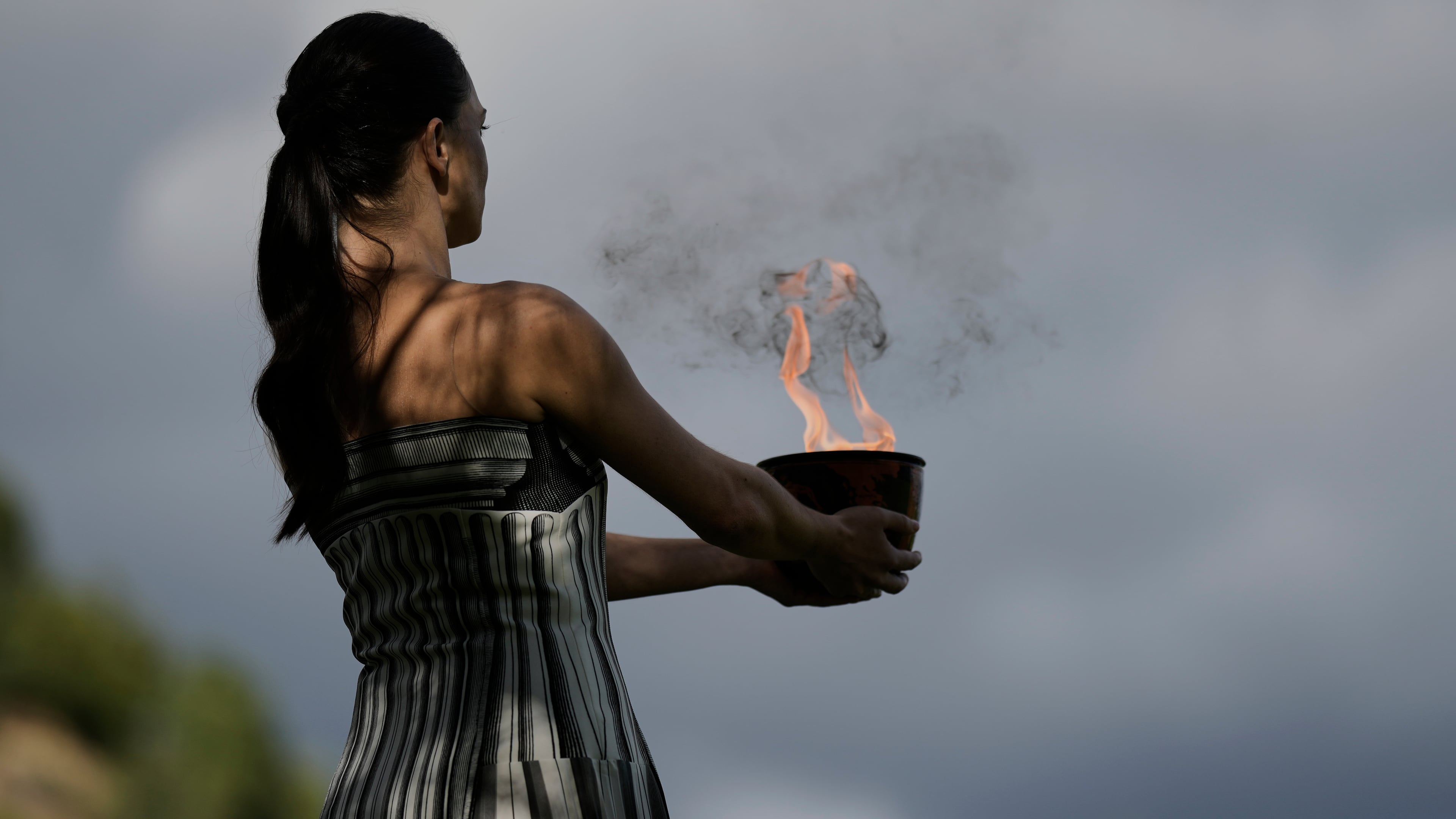 Actress Mary Mina, playing the high priestess holds a pot with the flame during a rehearsal ahead of the flame lighting for the Milan Cortina 2026 Winter Olympics, at the Ancient Olympia site, Greece, Monday, Nov. 24, 2025. (AP Photo/Petros Giannakouris)