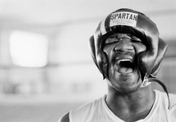 FILE - George Foreman laughs under his headgear at N'Sele, Zaire , after he boxed the first sparring rounds, Oct. 15, 1974. (AP Photo/Horst Faas, File)