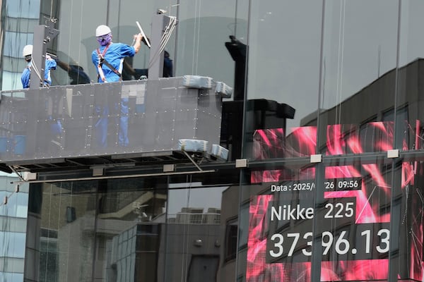 Workers clean the glass window of a building in front of an electronic stock board showing Japan's Nikkei index at a securities firm Monday, May 26, 2025, in Tokyo. (AP Photo/Eugene Hoshiko)