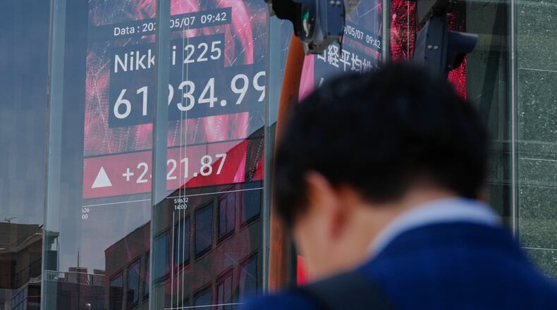 FILE - A person stands in front of an electronic stock board showing Japan's Nikkei index, seen through the glass wall of an office building in Tokyo, May 7, 2026. (AP Photo/Eugene Hoshiko, File)