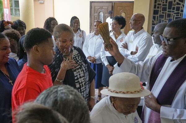 Rev. Leonvil Canois sprinkles with blessed water the faithful as they line up to enter Notre Dame d'Haiti Catholic church for a Lent revival service, March 29, 2025 in Miami. (AP Photo/Giovanna Dell'Orto)