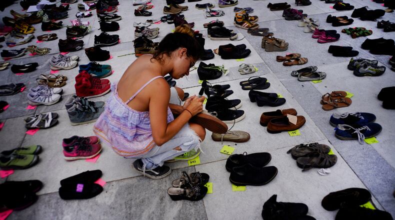 A woman places one of the hundreds of shoes in memory of those killed by Hurricane Maria in front of the Puerto Rico Capitol, in San Juan, Friday, June 1, 2018.  Puerto Rico's Institute of Statistics announced that it has sued the U.S. territory's health department and demographic registry seeking to obtain data on the number of deaths following Hurricane Maria as a growing number of critics accuse the government of lacking transparency.