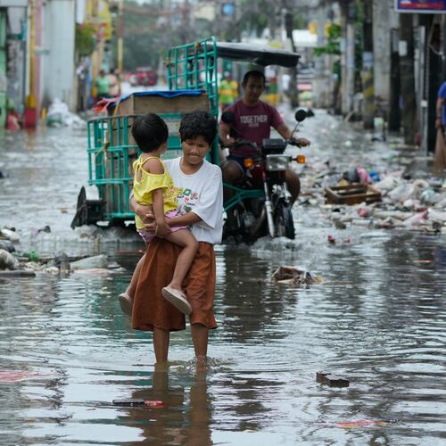 FILE - A woman and child crosses a flooded street due to Typhoon Fung-wong and high tide on Nov. 10, 2025, in Navotas, Philippines. (AP Photo/Aaron Favila, File)