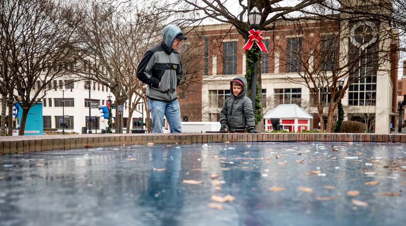 Bradley Thomas and his 5-year-old son, Briland, stand beside a frozen fountain on the Marietta Square on Monday, New Year’s Day. (Branden Camp / for the AJC)