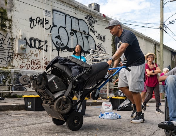 Cornelius Taylor's cousin Derek Chaney moves an electric wheelchair for an unhoused person as they are relocated to The Welcome House from Old Wheat Street.  (Ben Hendren for the AJC)