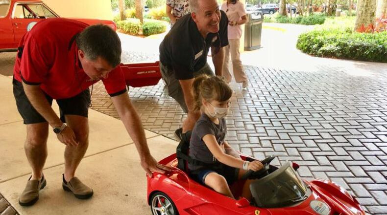 Brian Murphy, left, and Craig Kelley roll a mini-Ferrari convertible carrying 5-year-old Abigail Sporke into Palms West Hospital. Murphy and Kelley are with Little Smiles, which donated the car to the hospital's pediatric patients.