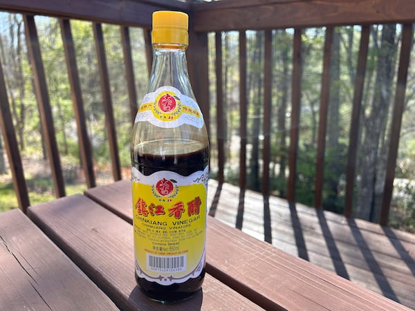 A bottle of vinegar is placed on a wooden table outside.