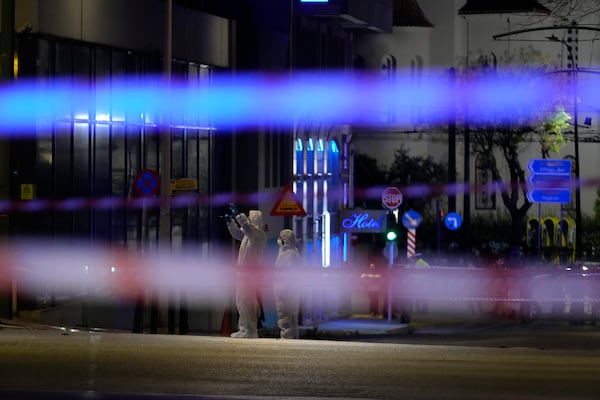 Police investigators wearing coveralls inspect the site after a bomb explosion outside of the Hellenic Train offices the company that runs Greece's railway, the first building on the left, in Athens, Greece, Friday, April 11, 2025. (AP Photo/Petros Giannakouris)